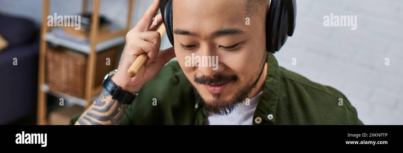 Ein hübscher asiatischer Mann, der Kopfhörer trägt und Drumsticks in einem Studio hält. Stockfoto