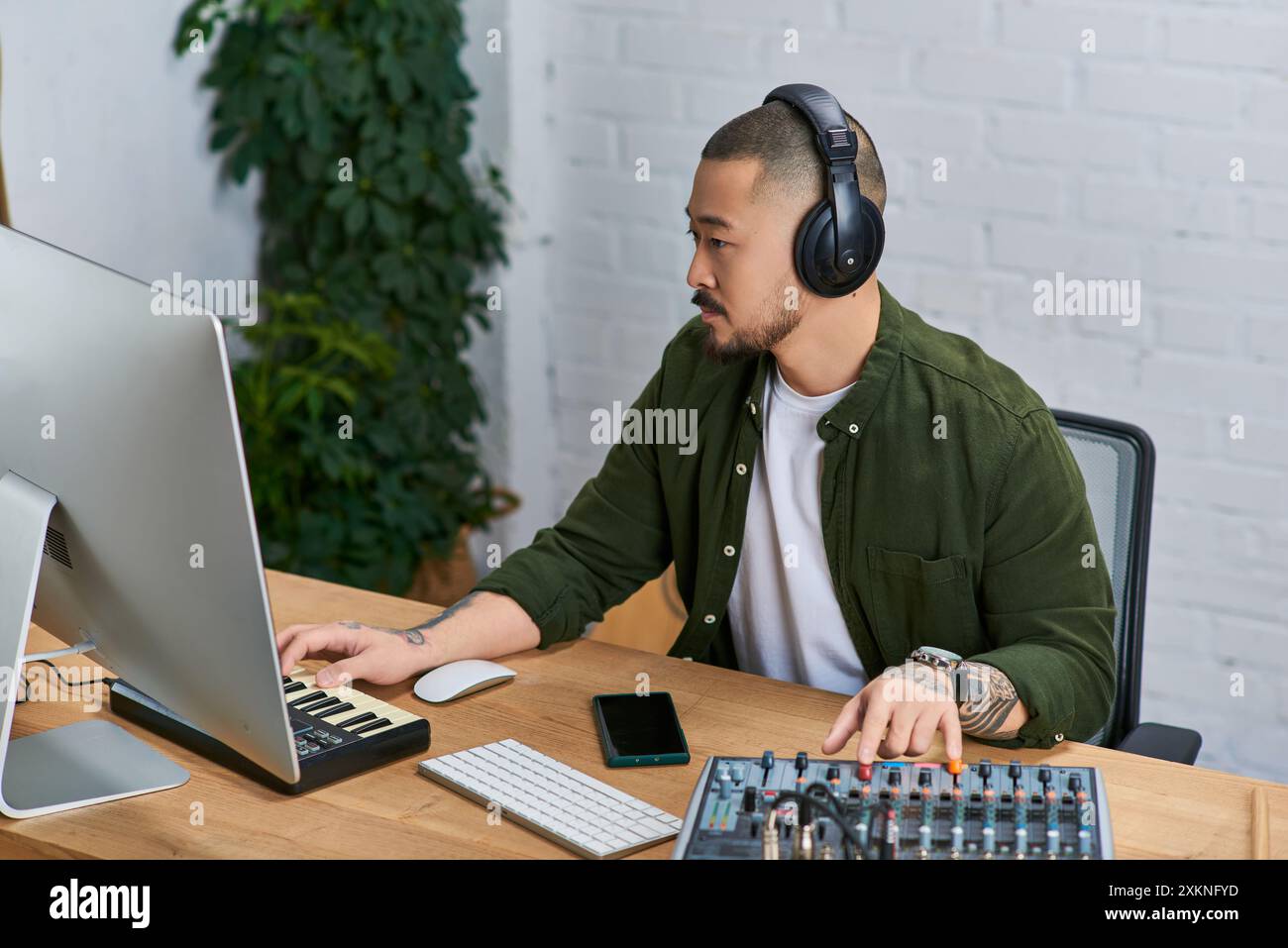 Ein gutaussehender asiatischer Mann, der Kopfhörer trägt, arbeitet an einem Musikprojekt in seinem Studio. Stockfoto