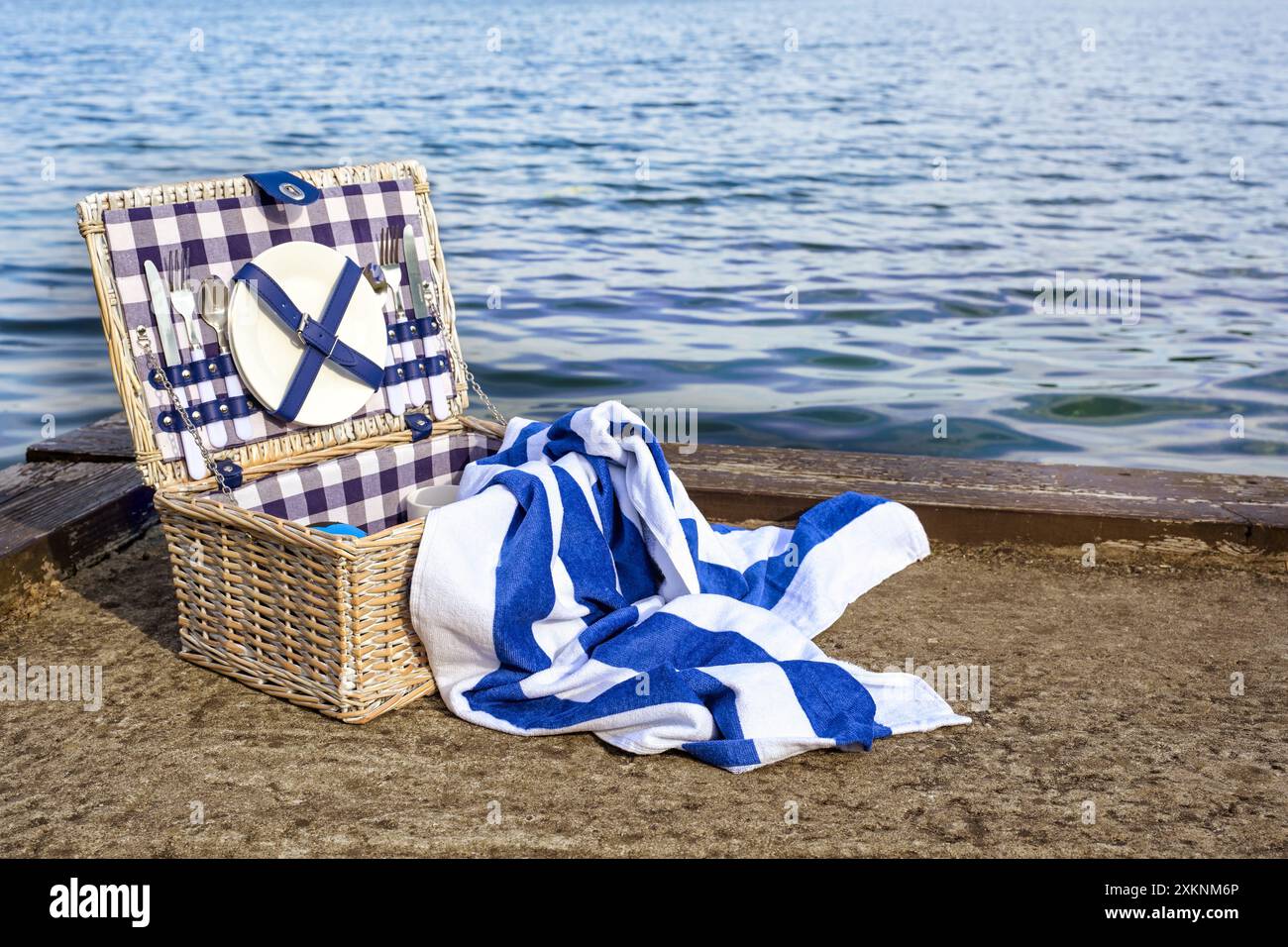 Badeausflug im Urlaub oder am Wochenende mit Picknickkorb und blauweiß gestreiftem Handtuch am Kai am Meer an einem sonnigen Tag, Kopierraum Stockfoto