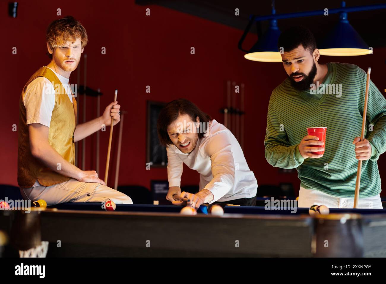 Freunde spielen eine freundliche Partie Billard in einem schwach beleuchteten Raum. Stockfoto
