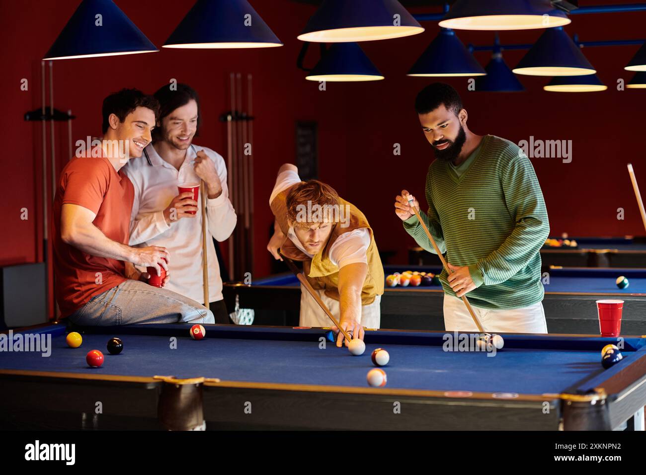 Freunde spielen Billard in einem schwach beleuchteten Raum, lässig gekleidet und haben Spaß. Stockfoto