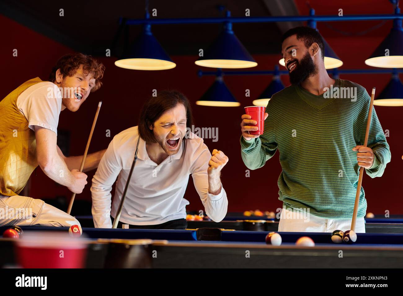 Freunde feiern einen Sieg am Pool in einem schwach beleuchteten Raum. Stockfoto