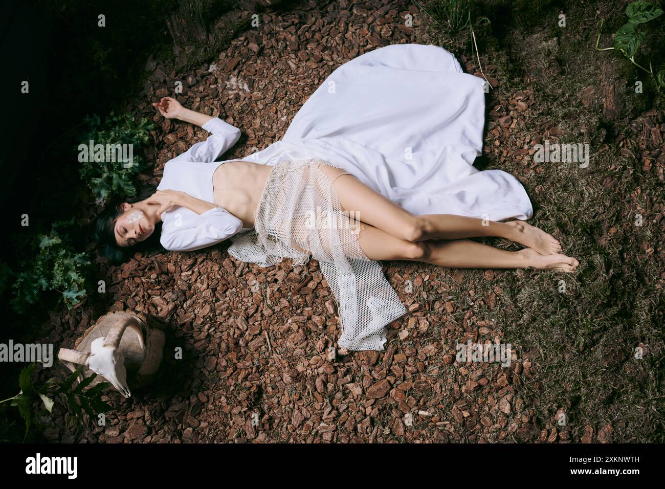 Eine Frau in einem weißen Kleid liegt auf dem Boden und auf dem Laub. Stockfoto