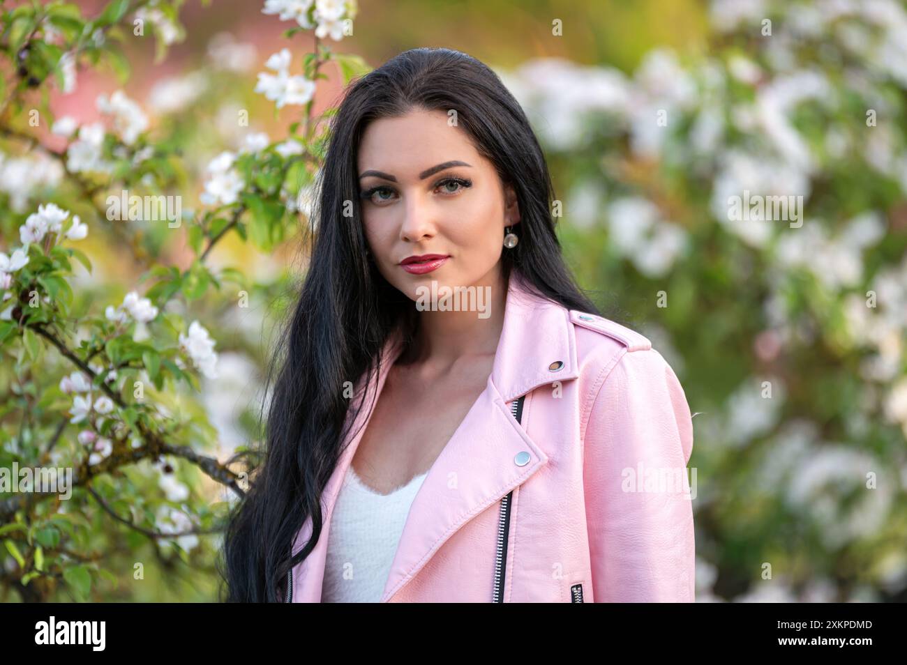 Eine Frau in rosa Jacke lächelt neben einem blühenden Baum. Geringe Tiefe von feld Stockfoto