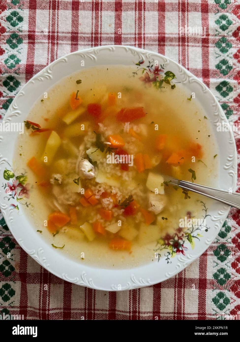 Hausgemachte Hühnersuppe in einer floralen Keramikschale auf einer karierten Tischdecke. Rumänisches Essen von ungarischen Ethnien. Stockfoto