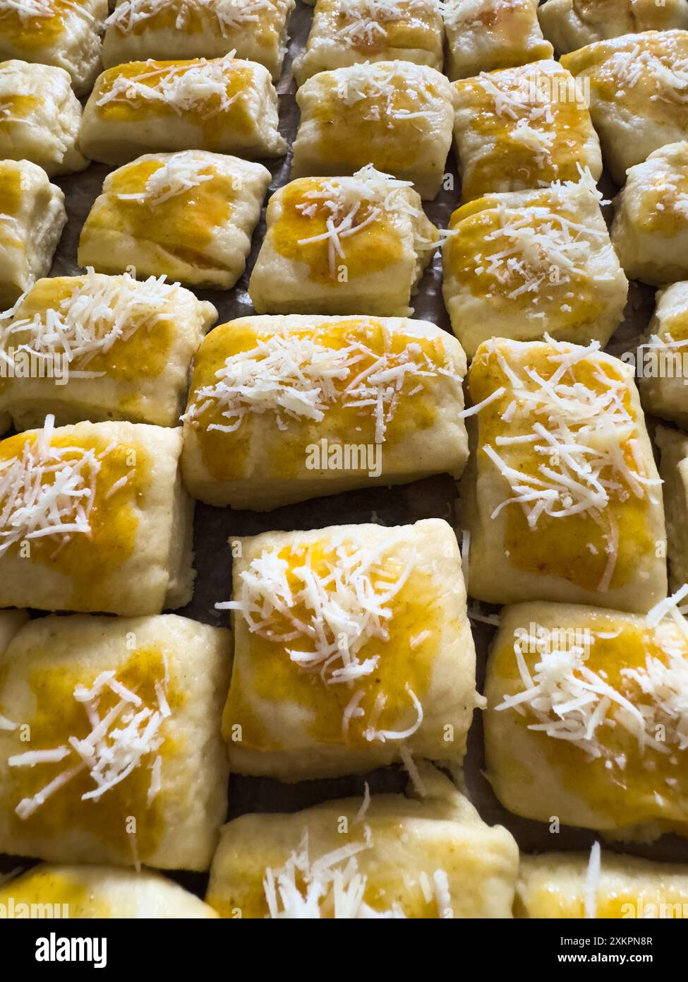 Hausgemachte, frisch zubereitete Gebäckstücke mit geriebenem Käse und Eierwaschmittel zum Backen Stockfoto