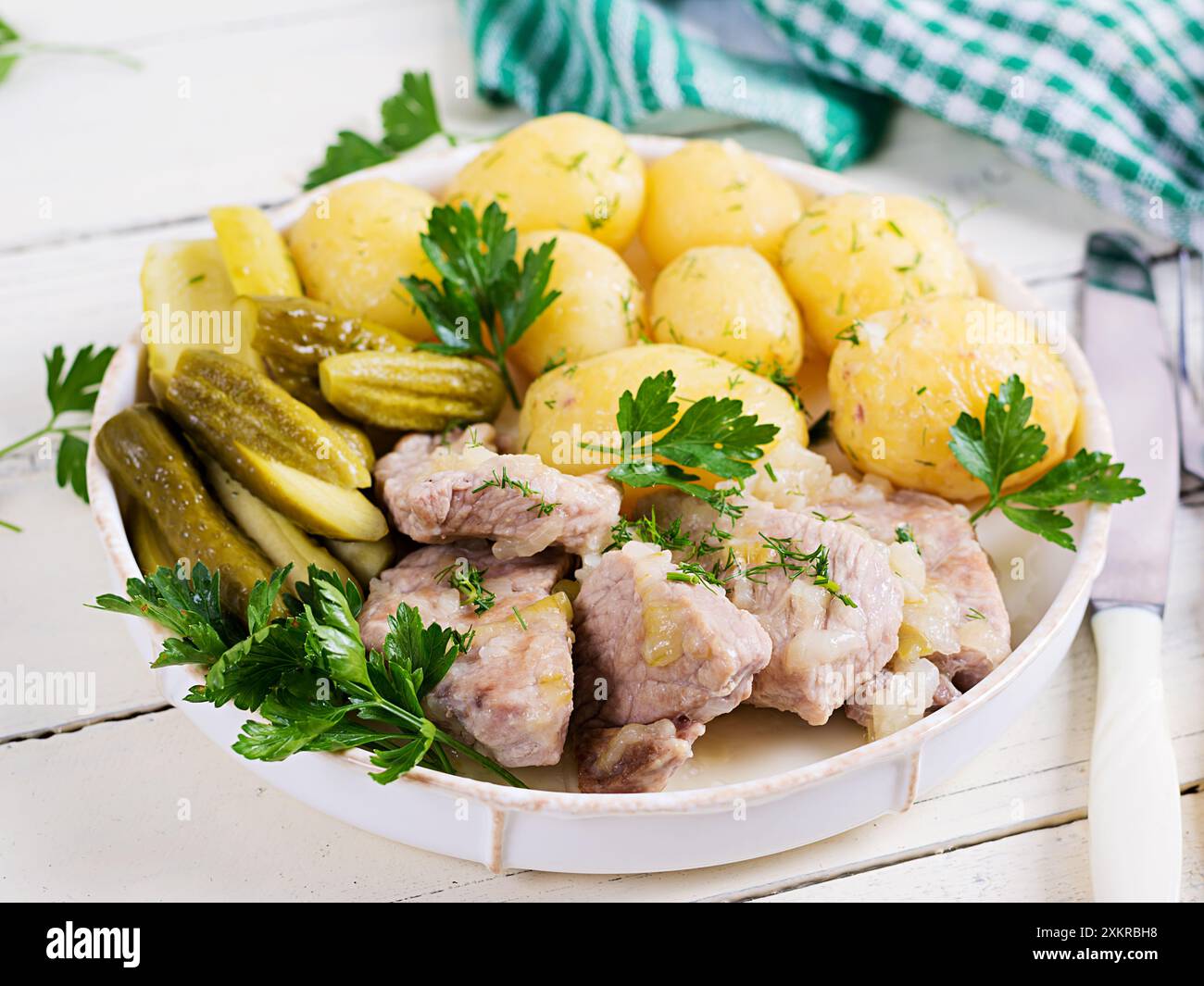 Gekochte neue Kartoffeln mit Stücken gedünstetem Schweinefleisch und eingelegten Gurken. Einfaches Essen. Ländliches Essen. Leckeres Essen. Mittagessen Stockfoto