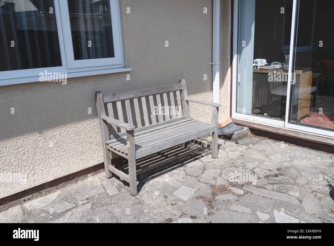 Eine Holzbank im Hinterhof eines Hauses in der Nähe der Terrassentür Stockfoto