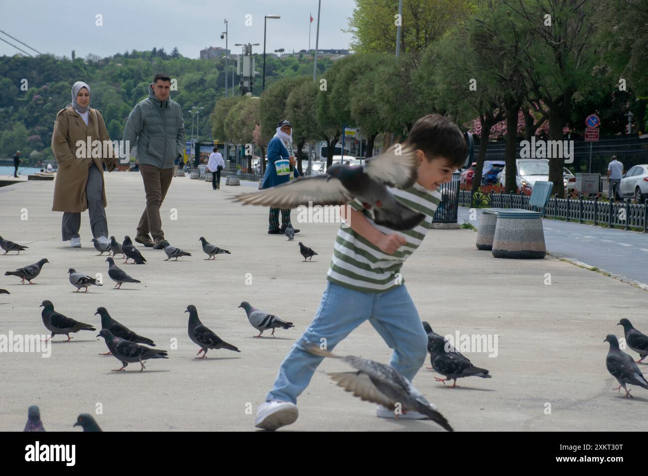 18.04.2024, Istanbul, Türkei: Junge jagt Tauben und Bosporus im Hintergrund. Stockfoto