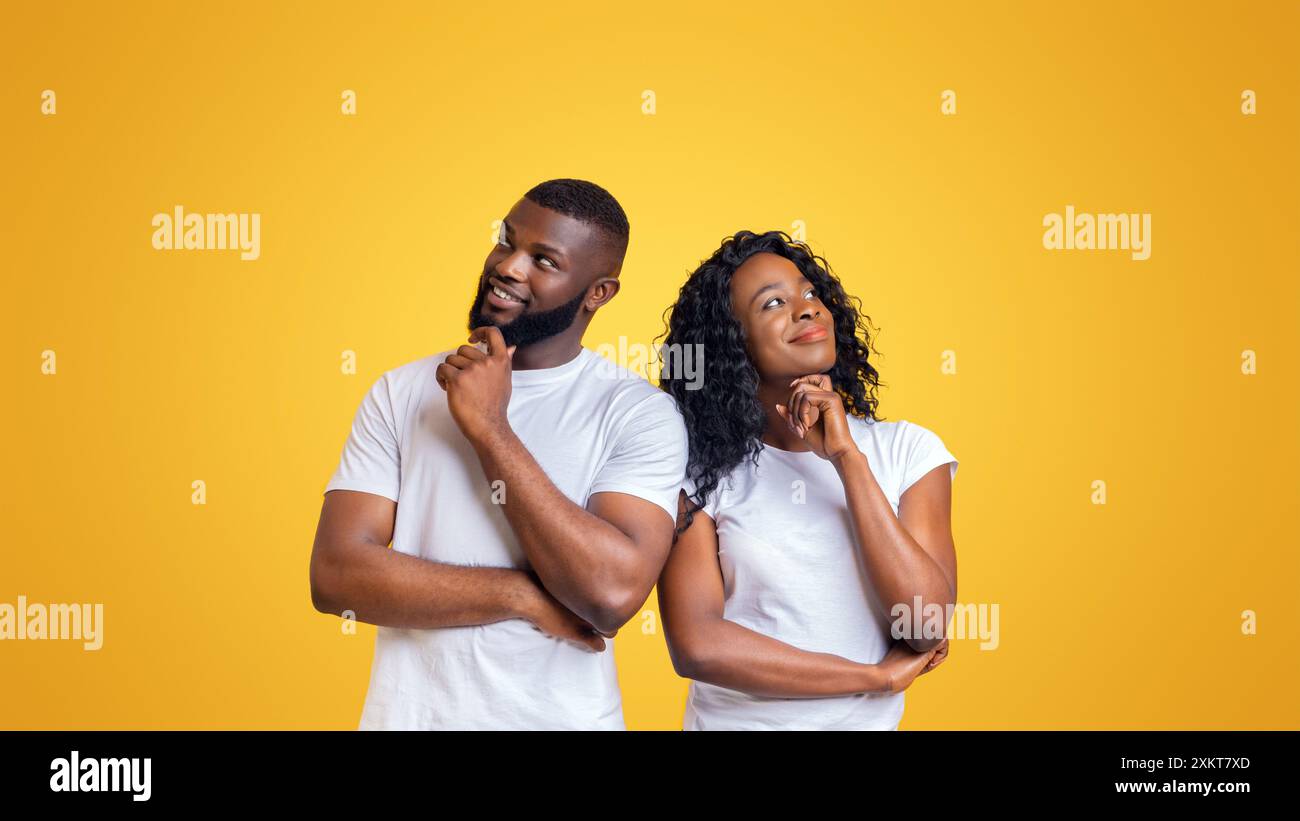 Ein Mann und eine Frau, beide mit dunkler Haut, stehen Seite an Seite vor einem leuchtend gelben Hintergrund und blicken nachdenklich nach oben mit den Händen auf ihrem Chi Stockfoto