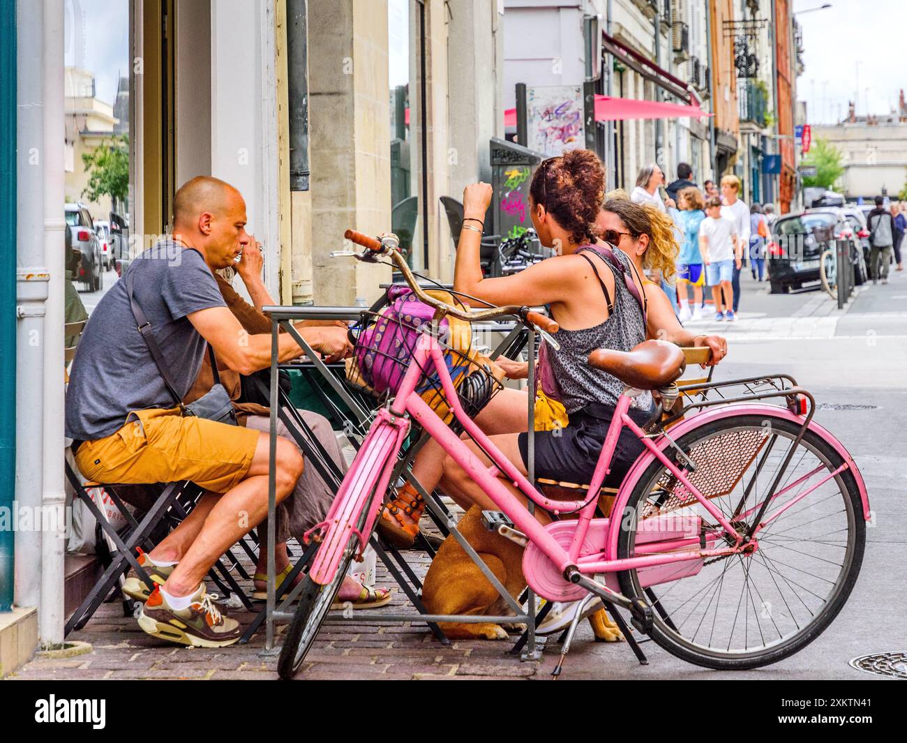 Gemischte Gruppe von Freunden (einer mit rosafarbenem Fahrrad), die am Kaffeetisch in der Fußgängerzone sitzen - Tours, Indre-et-Loire (37), Frankreich. Stockfoto