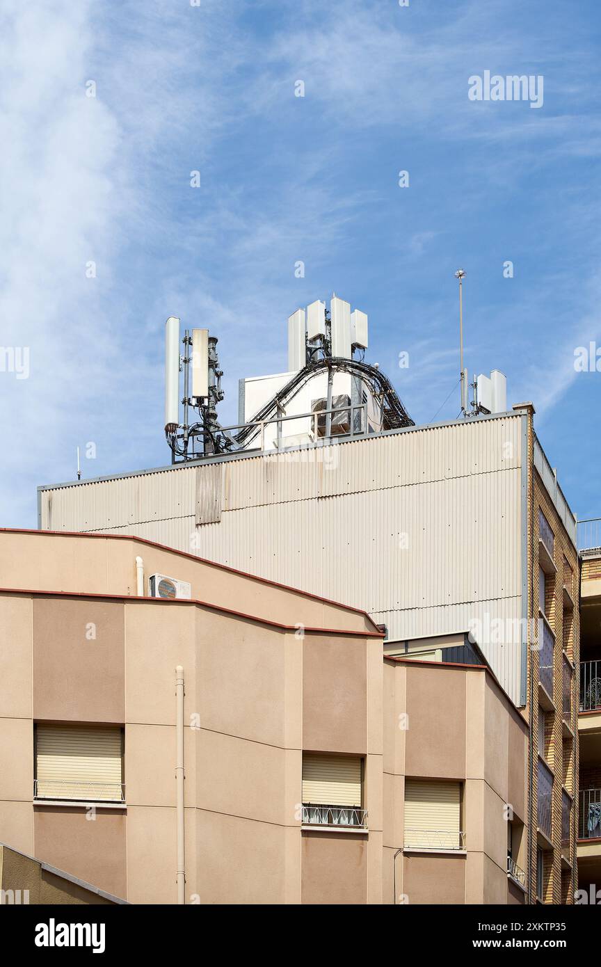 Bild von Telekommunikationsantennen auf dem Dach eines modernen Gebäudes vor blauem Himmel, die die Integration von Technologie in die städtische Umgebung betonen Stockfoto