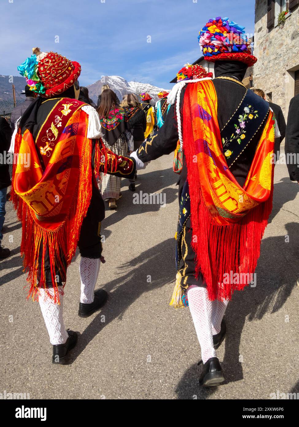 Balari spazieren durch die Bagolino Straßen während des Karnevals, in der traditionellen Tracht mit einem Gesicht, das mit einer elfenbeinfarbenen und schwarzen Maske bedeckt ist, und Kopf unter einem Filzhut, der mit rotem Band bedeckt ist, mit Goldschmuck und bunten Bändern, die eine Schleife bilden Stockfoto