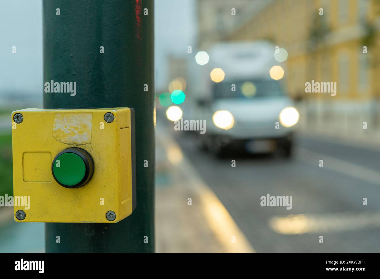 Grüner Knopf mit gelbem Rahmen zum Stoppen des Verkehrs auf einem Quersteg mit verschwommenem Hintergrund Stockfoto