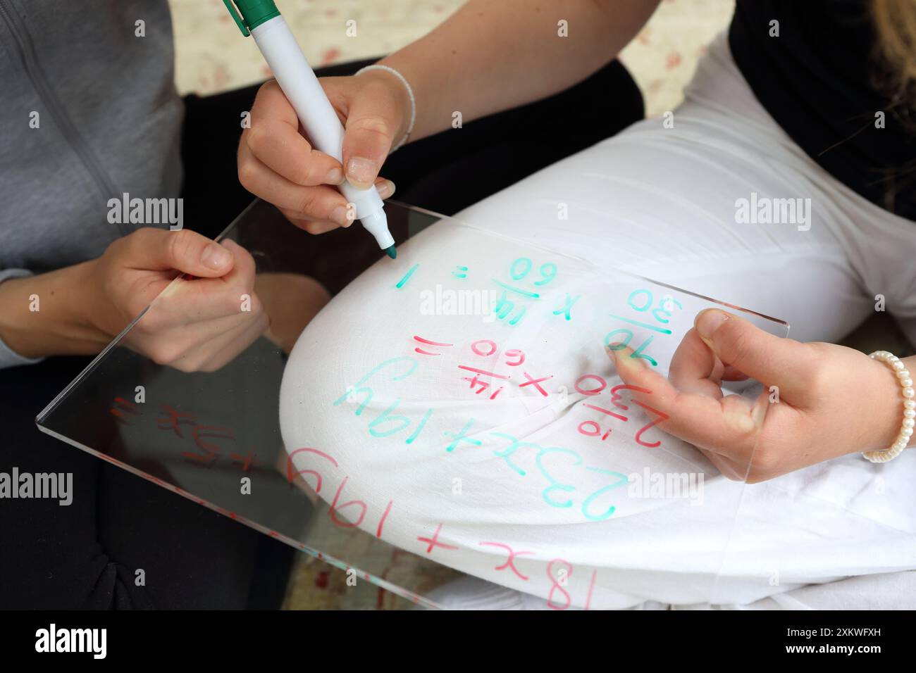 Mädchen, die Mathematik machen, sitzen auf dem Boden, schreiben auf Whiteboard mit Stiften Algebra Fraktionen Mathematik Schwestern Mathematik Bildung Mädchen in MINT Stockfoto