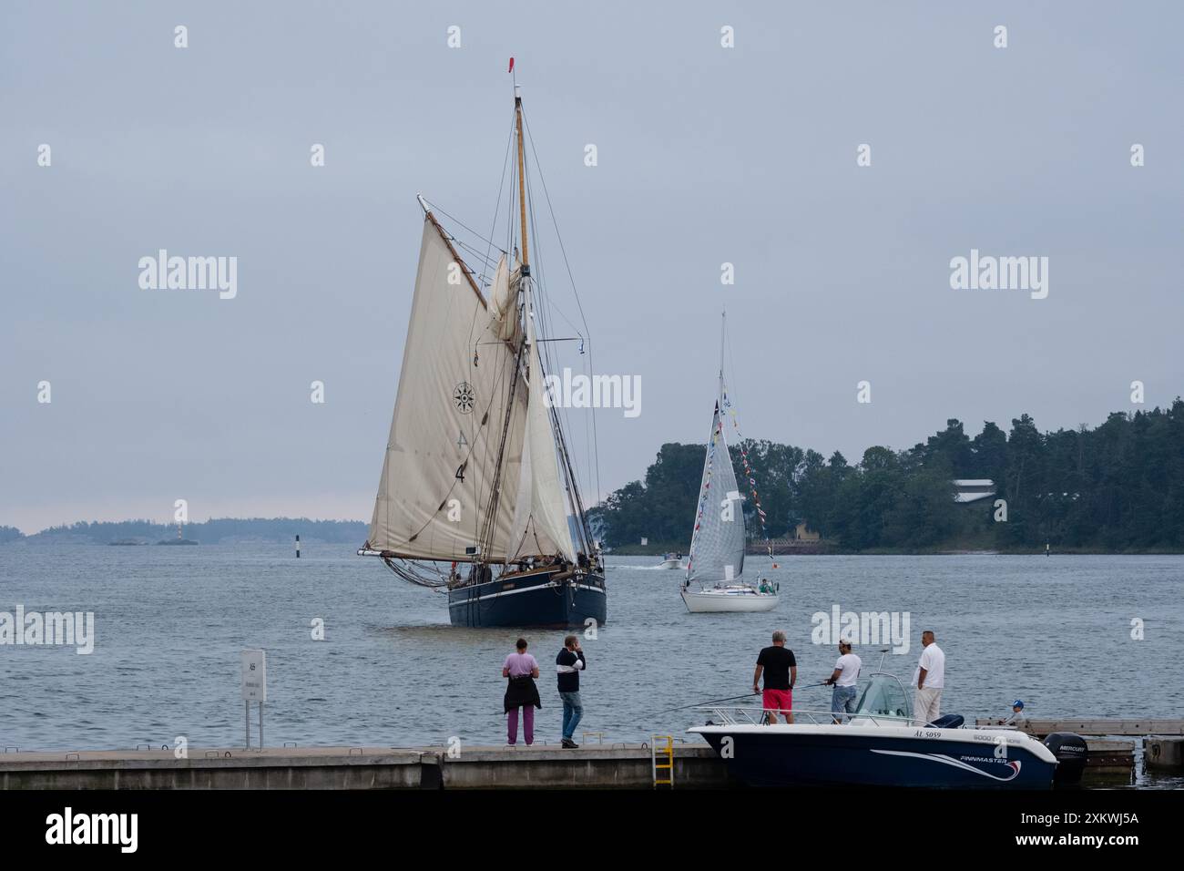 MARIEHAMN, Åland, FINNLAND - 23. JULI 2024: Die Menschen stehen und beobachten, wie das Großschiff Dankbarkeit eines der ersten war, die am Abend vor dem Eröffnungstag im Haupthafen von Mariehamn ankamen. Tag 1 der dreitägigen Åland-Etappe des Tall Ships Race 2024 im Haupthafen, Mariehamn, Åland, Finnland. Foto: Rob Watkins/Alamy Live News. INFO: Das Tall Ships Race ist eine jährliche Segelveranstaltung mit historischen und modernen Großschiffen. Es fördert internationale Freundschaft und Jugendausbildung und zieht Teilnehmer und Zuschauer weltweit an, um maritimes Erbe und die Kunst des traditionellen Segelns zu feiern. Stockfoto