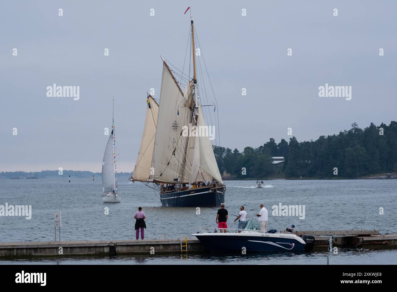 MARIEHAMN, Åland, FINNLAND - 23. JULI 2024: Die Menschen stehen und beobachten, wie das Großschiff Dankbarkeit eines der ersten war, die am Abend vor dem Eröffnungstag im Haupthafen von Mariehamn ankamen. Tag 1 der dreitägigen Åland-Etappe des Tall Ships Race 2024 im Haupthafen, Mariehamn, Åland, Finnland. Foto: Rob Watkins/Alamy Live News. INFO: Das Tall Ships Race ist eine jährliche Segelveranstaltung mit historischen und modernen Großschiffen. Es fördert internationale Freundschaft und Jugendausbildung und zieht Teilnehmer und Zuschauer weltweit an, um maritimes Erbe und die Kunst des traditionellen Segelns zu feiern. Stockfoto