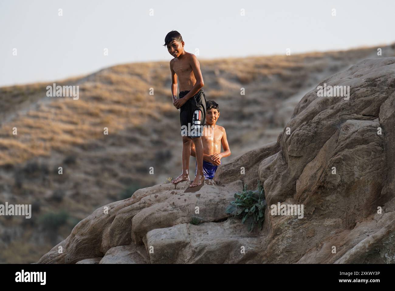 Mossul, Irak. Juli 2024. Feuchte Jungen auf den Felsen des Mosul-Stausees bei Namrik im Nordirak. Der Mosul-Staudamm, früher Saddam-Staudamm, ist der größte Staudamm des Irak, der sich am Tigris-Fluss in Ninive oberhalb von Mosul befindet. Es erzeugt Wasserkraft und liefert Wasser für die nachgelagerte Bewässerung. Bei voller Kapazität fasst er 11,1 Kubikkilometer (2,7 Kubikmeilen) Wasser und versorgt die 1,7 Millionen Einwohner Mosuls mit Strom. (Foto: Ismael Adnan/SOPA Images/SIPA USA) Credit: SIPA USA/Alamy Live News Stockfoto