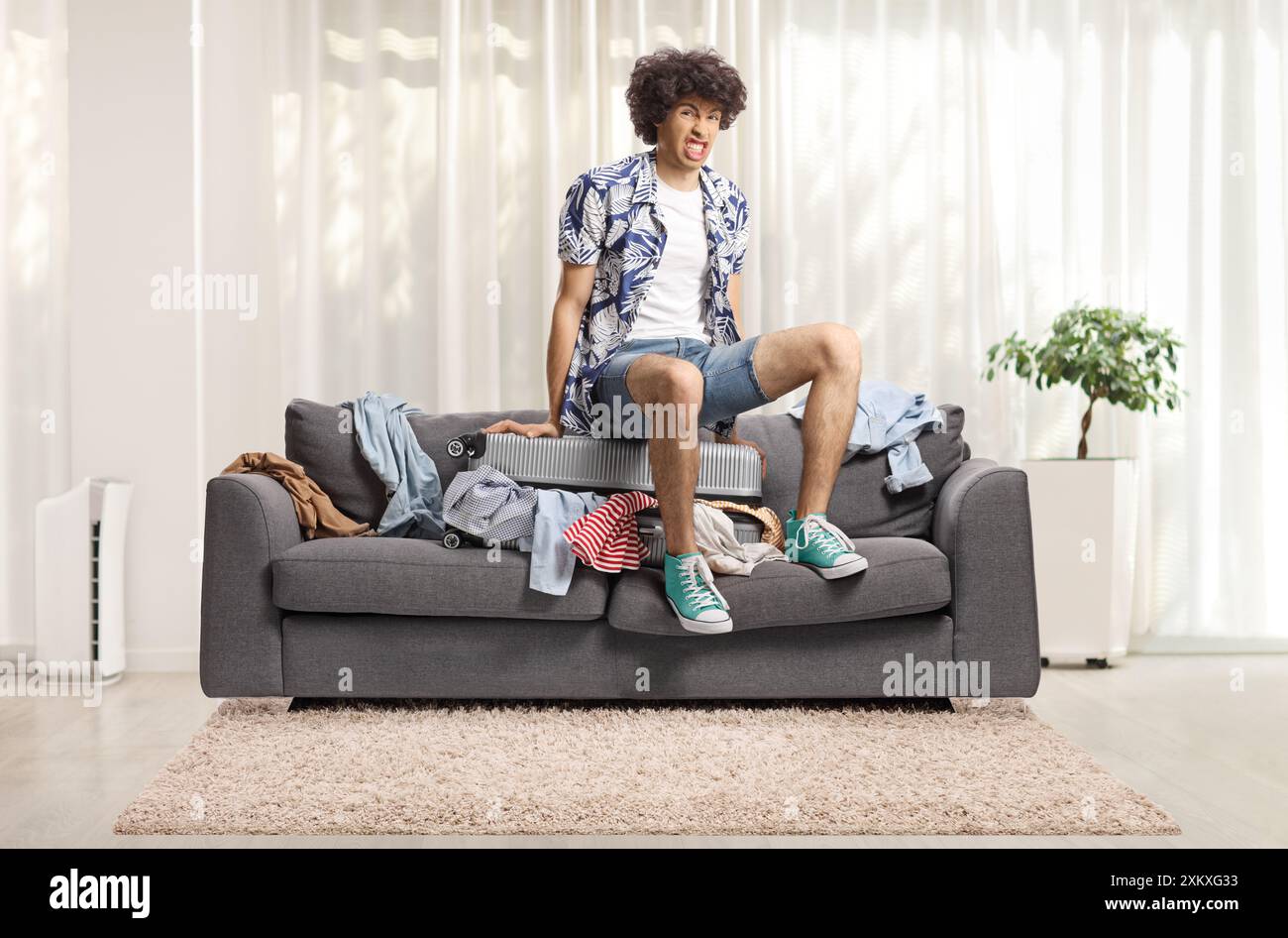 Junger Mann, der zu Hause einen Koffer auf ein Sofa drückt Stockfoto