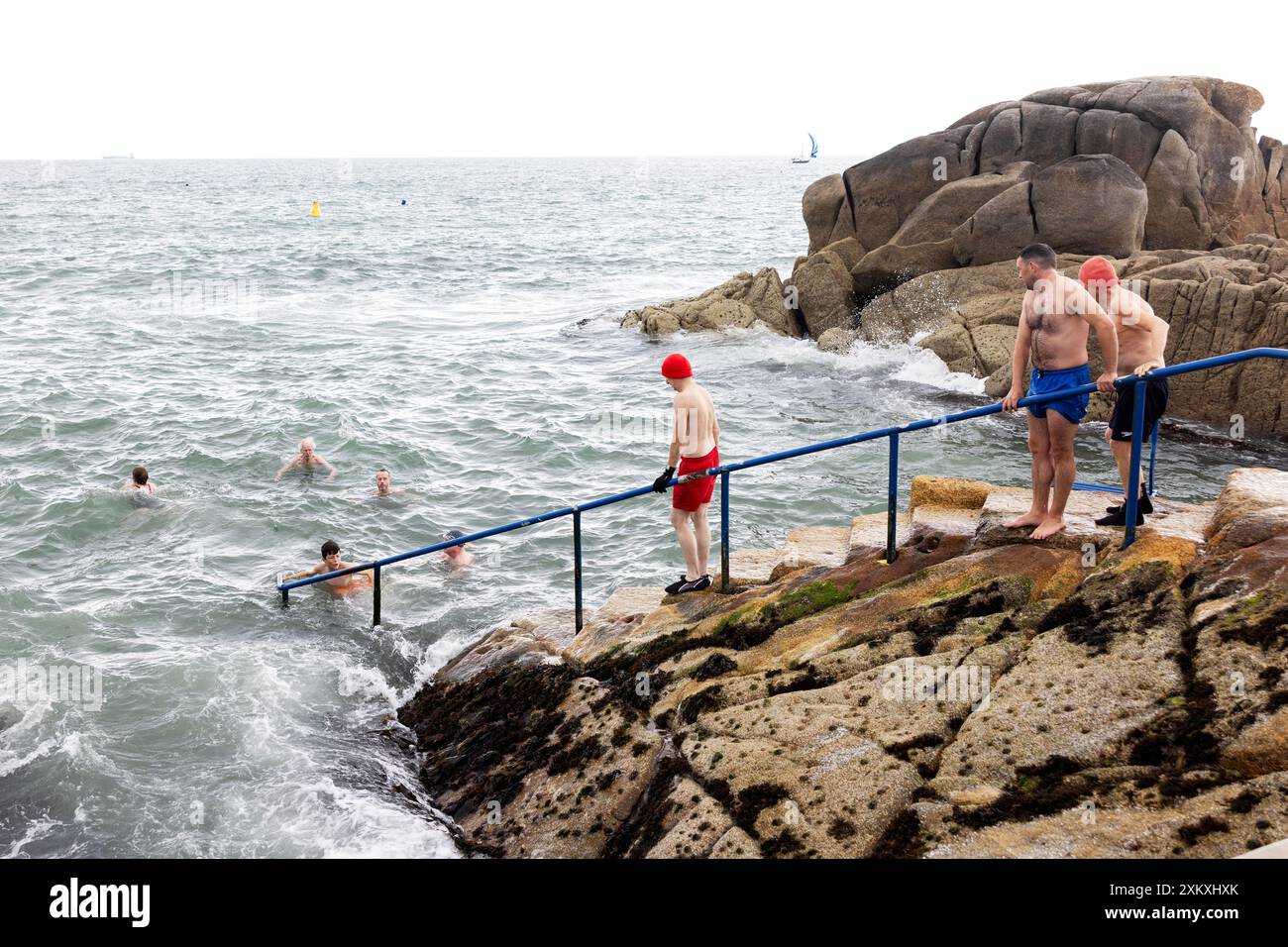 Eine Gruppe von Männern und Frauen tritt ein und schwimmt im kalten Wasser der Irischen See am Forty Foot Swimming Hole in Sandycove, Dublin, Irland. Stockfoto
