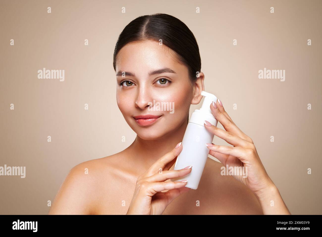 Eine junge Frau zeigt eine Flasche mit einem Schaumspender zum Waschen. Tägliche Kosmetikwerbung für Hautpflege. Studio Shoot Beige Hintergrund Stockfoto