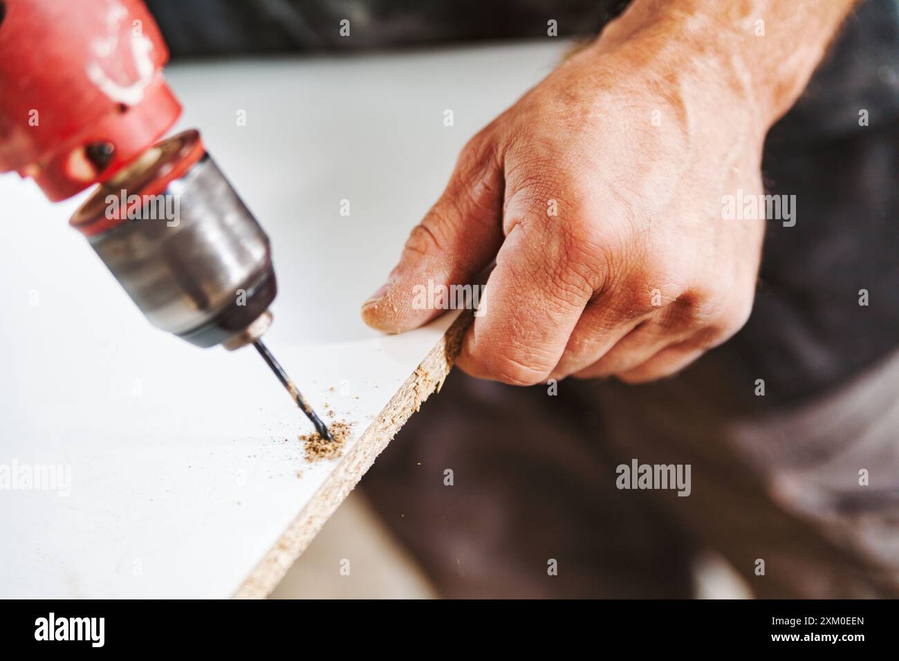 Ein fokussierter Zimmermann bohrt ein Loch in eine weiße Planke und erzeugt Sägemehl. Hingabe und Präzision sind der Schlüssel in seinem Handwerk Stockfoto