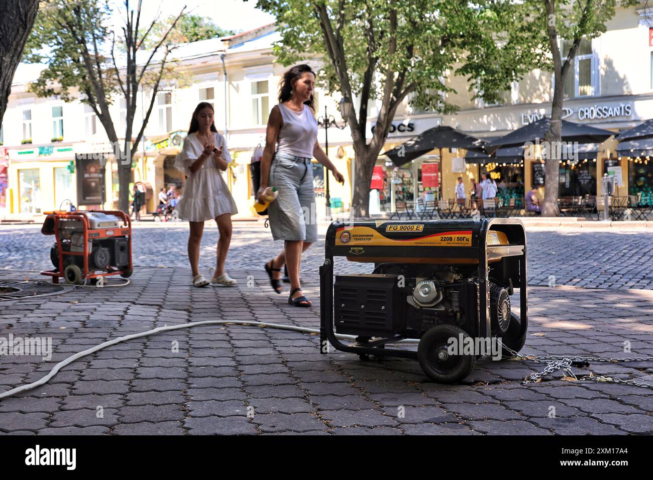 ODESA, UKRAINE - 23. JULI 2024 - Frauen gehen an Dieselgeneratoren vorbei, die bei Stromausfällen in Odesa, Südukraine, als Backup genutzt werden. Stockfoto
