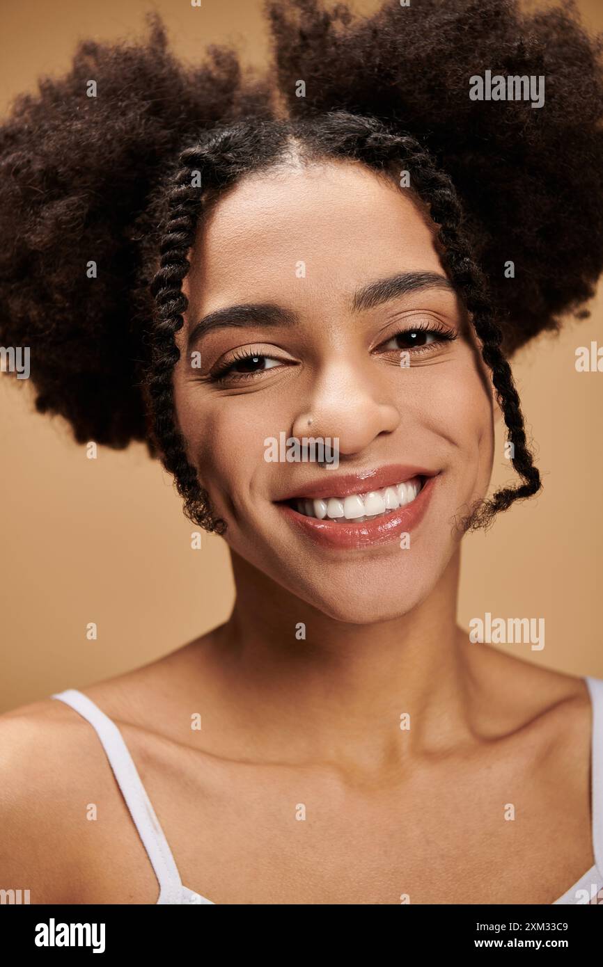 Eine junge Afroamerikanerin lächelt strahlend vor beigefarbenem Hintergrund. Stockfoto