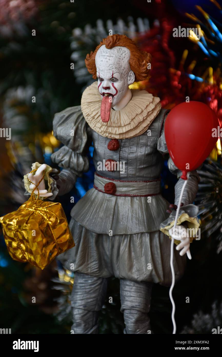 NECA Actionfigur von Pennywise Clown aus dem Horrorfilm IT. Gruseliges Spielzeug mit aufgehängter Zunge, Miniatur-Geschenkbox, roter Ballon. Weihnachtsbaum. Stockfoto