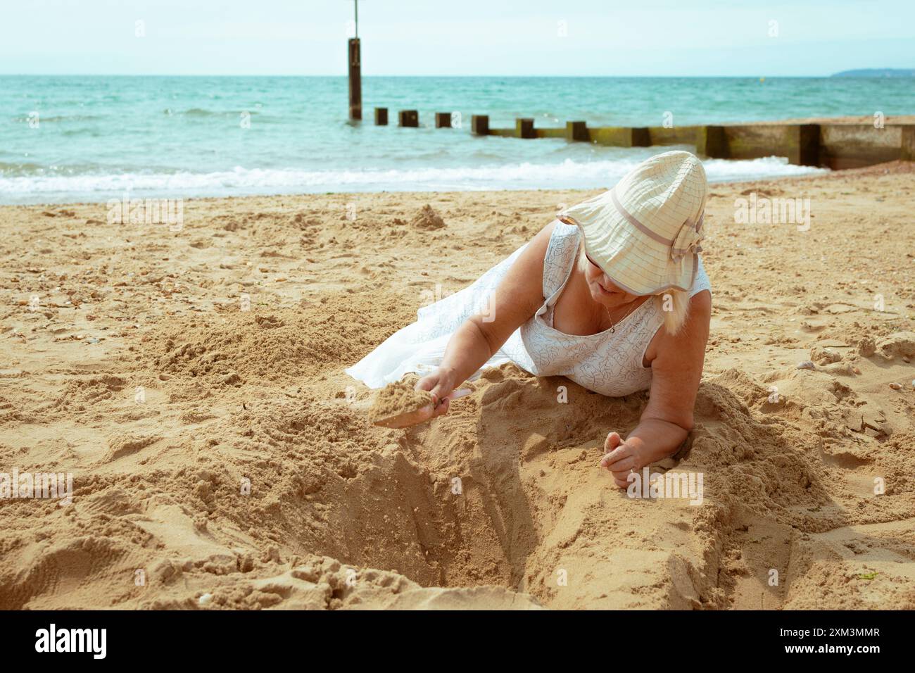 Reife Frau, die am Strand mit einem Spielzeugspaten in Sand gräbt, nie zu alt. Stockfoto