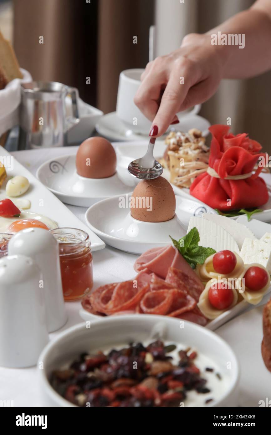 Eine junge Frau genießt das Frühstück im Hotel mit verschiedenen Speisen Stockfoto