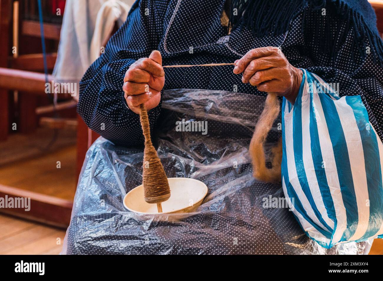 Hände einer Andenfrau, die braune Alpakafasern in einem angestammten Spinnrad in den Anden in einer handwerklichen Werkstatt dreht Stockfoto