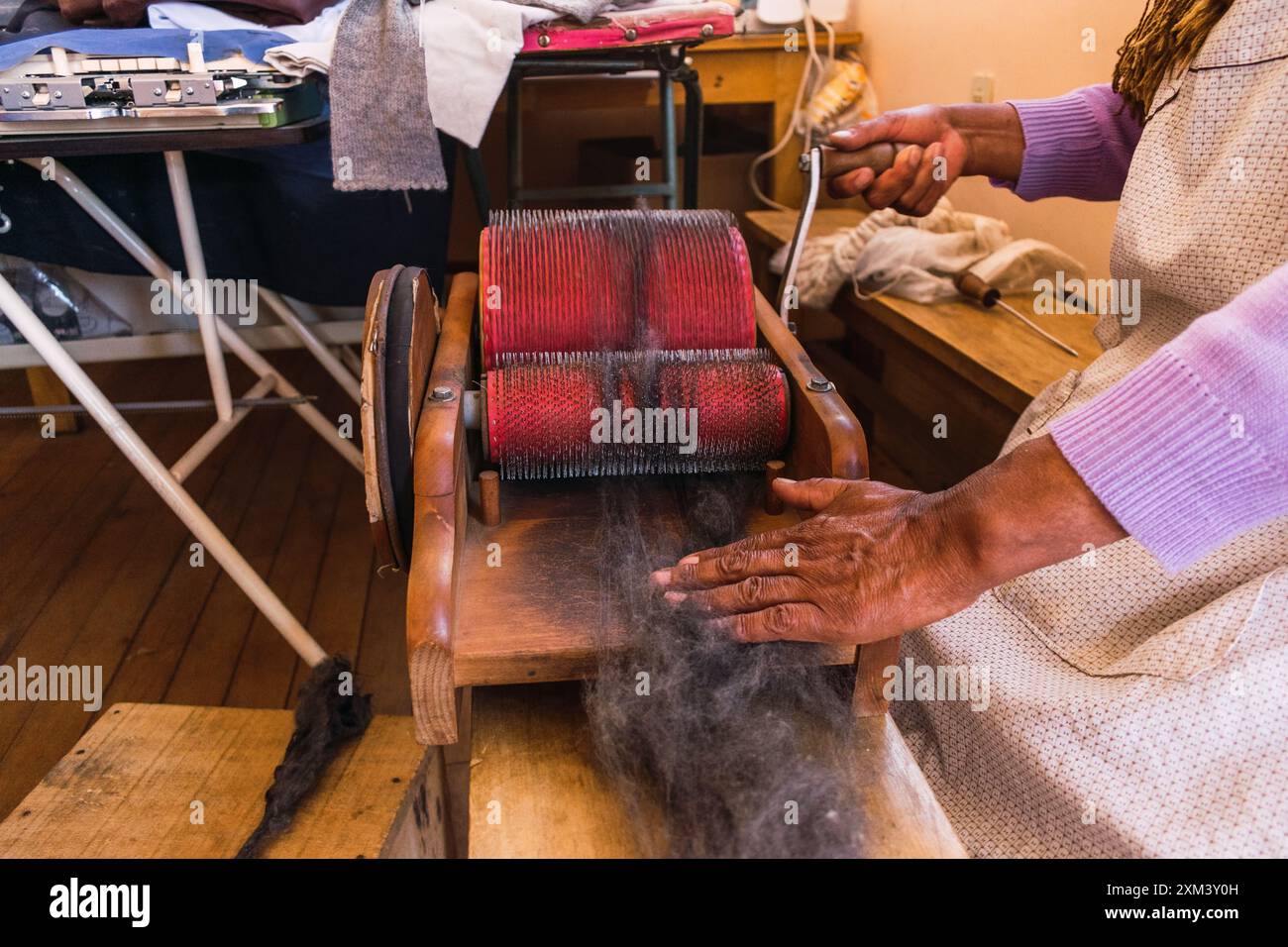 Hände einer Andenfrau, die braune Alpakafasern in einem angestammten Spinnrad in den Anden in einer handwerklichen Werkstatt dreht Stockfoto