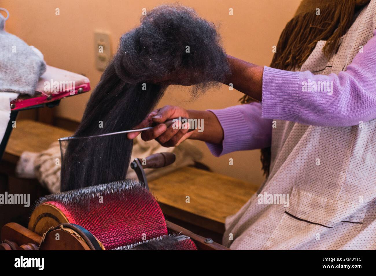 Hände einer Andenfrau, die braune Alpakafasern in einem angestammten Spinnrad in den Anden in einer handwerklichen Werkstatt dreht Stockfoto