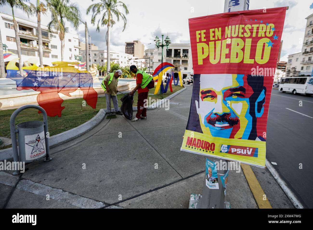 Caracas, Venezuela. Juli 2024. Straßenkehrer arbeiten im Hintergrund, während ein Wahlplakat für die Wiederwahl von Präsident Maduro und seiner PSUV-Partei im Vordergrund zu sehen ist. Am 28. Juli konnte der Staatschef nach elf Jahren an der Macht aus dem Amt gewählt werden. Quelle: Jeampier Arguinzones/dpa/Alamy Live News Stockfoto