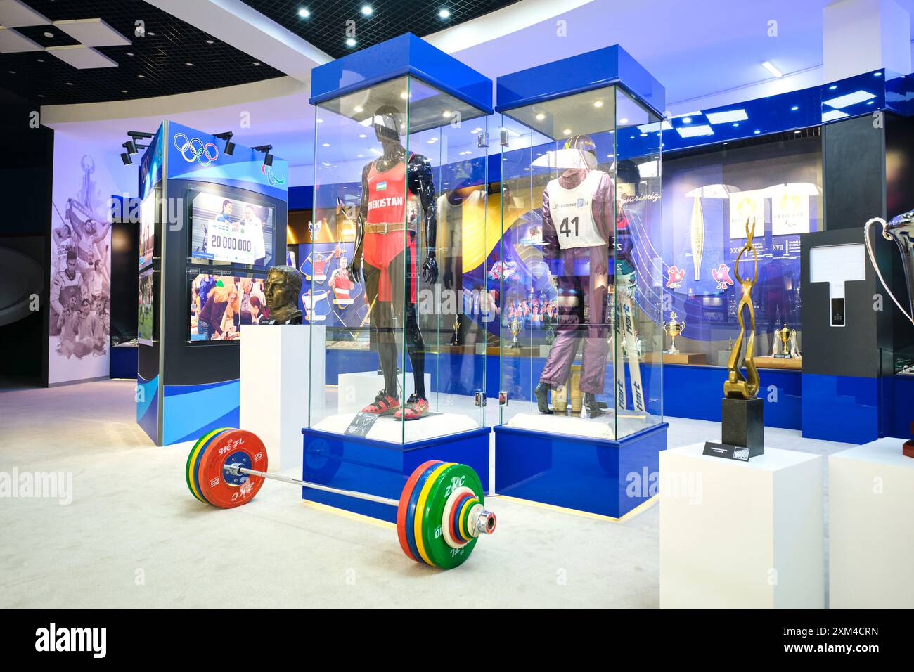 Fußbodenausstellung von Uniformen und eine Hantelstange aus Stahl. Im Museum für Olympischen Ruhm in Taschkent, Usbekistan. Stockfoto