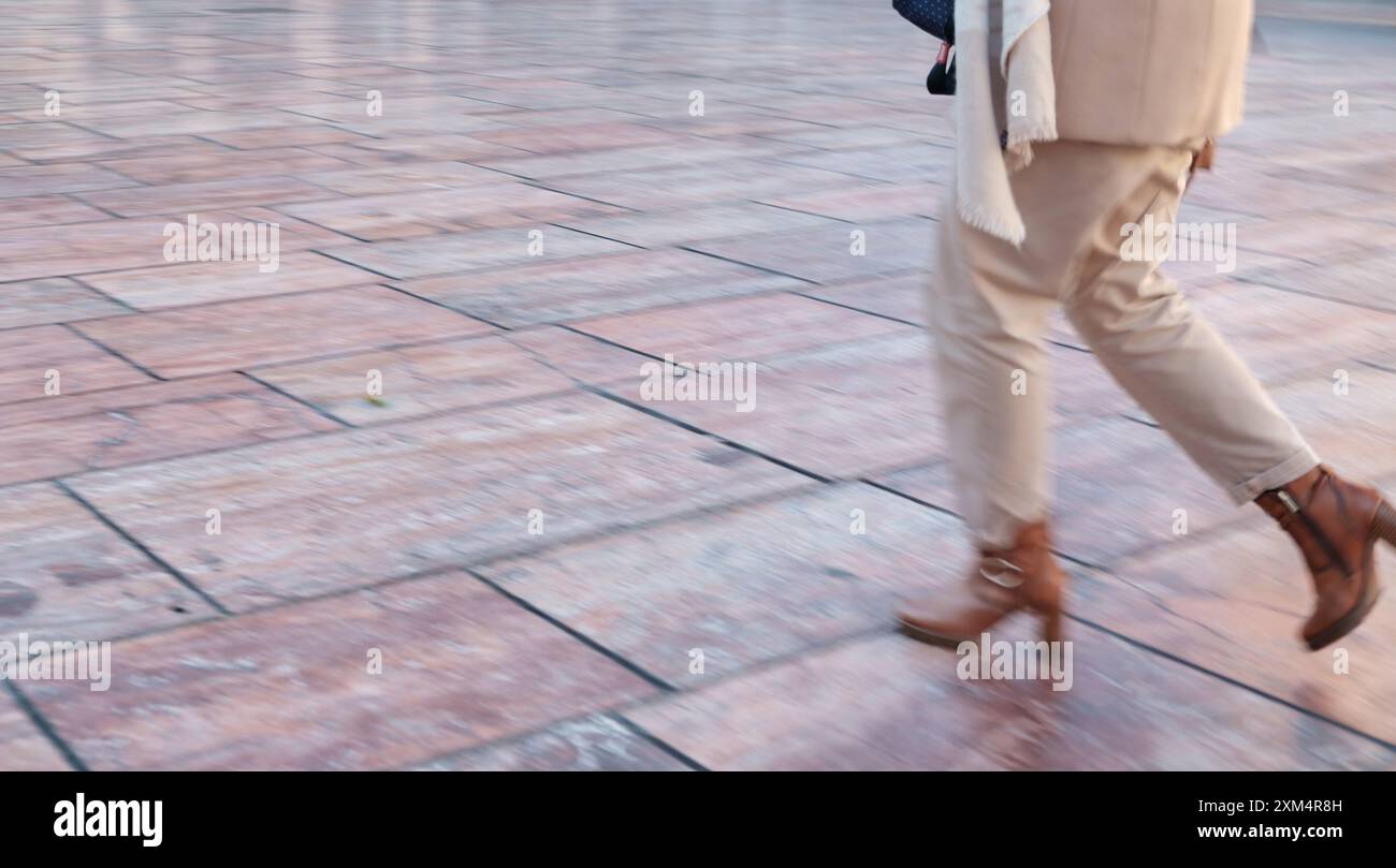 Überstürzen Sie Menschen. Verschwommene Bewegungen einer Person im mittleren Schritt auf einem gefliesten Boden, mit einer unteren Hälfte in hellen Hosen und braunen Schuhen Stockfoto