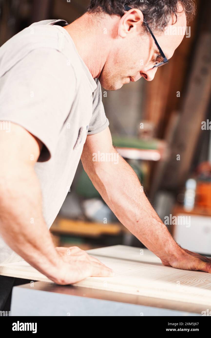 Der Zimmermann mit Schutzbrille glättet eine Holzdiele in seiner Werkstatt. Er nutzt seine Stärke und Erfahrung, um hochwertige Möbel herzustellen Stockfoto