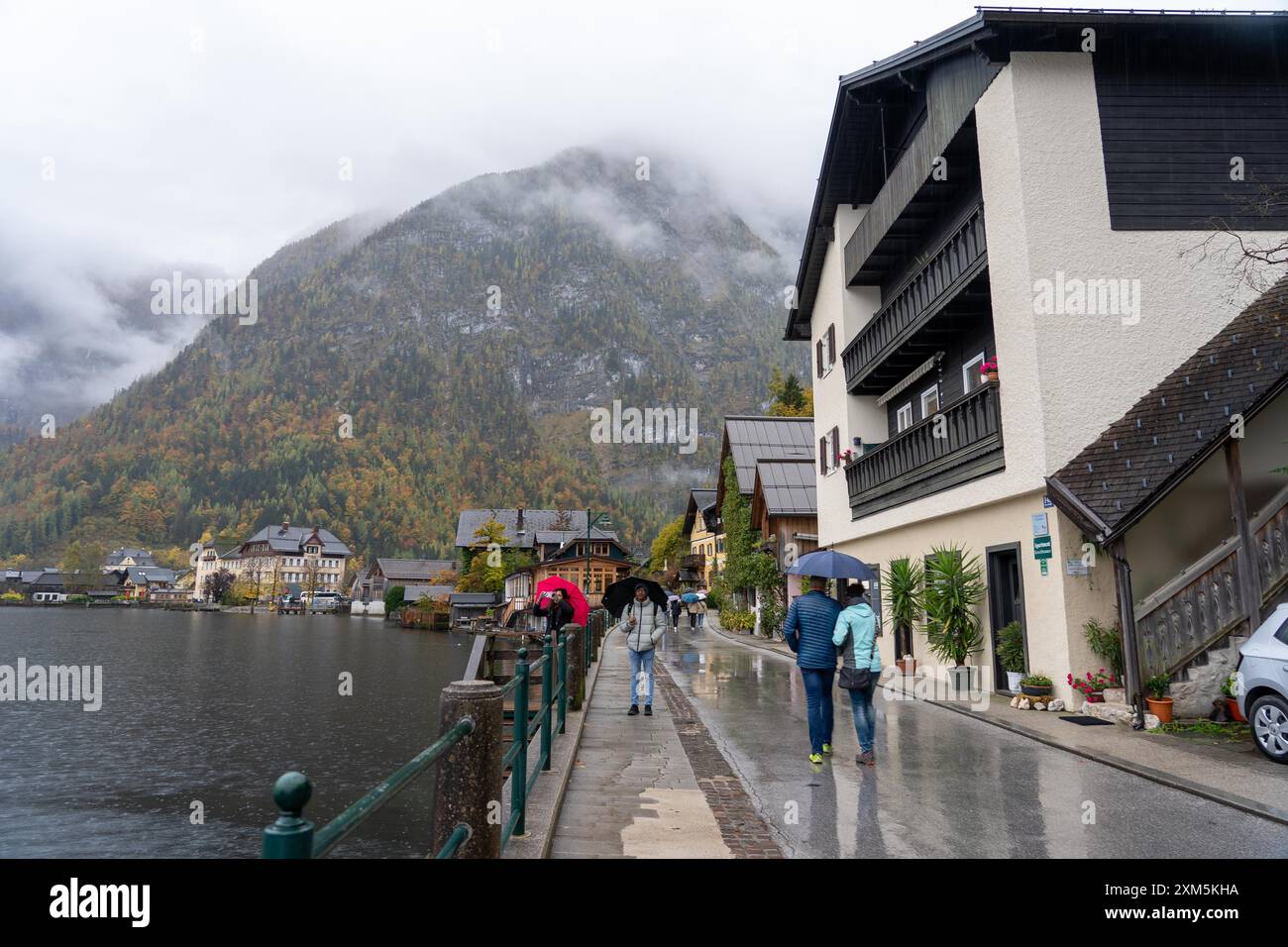 Hallstatt, Österreich - 31. Oktober 2023 : Regentag in Hallstatt, Österreich, mit Blick auf See und Berge. Die Leute laufen die Straße entlang mit Umbr Stockfoto