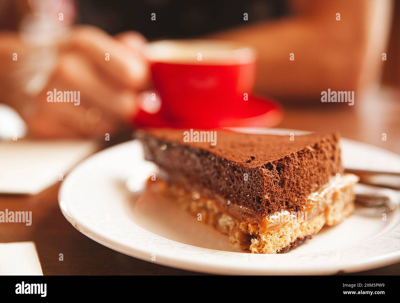 Appetitliches Schokoladenstück und Mann mit einer Tasse roten Kaffees auf verschwommenem Hintergrund Stockfoto