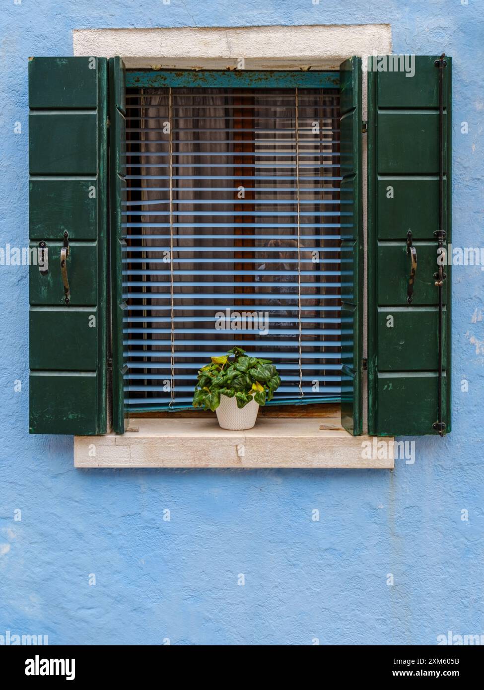 Das sanfte hellblaue Fenster strahlt einen ruhigen Charme aus und fügt sich harmonisch in die ruhige Atmosphäre von Burano ein. Stockfoto