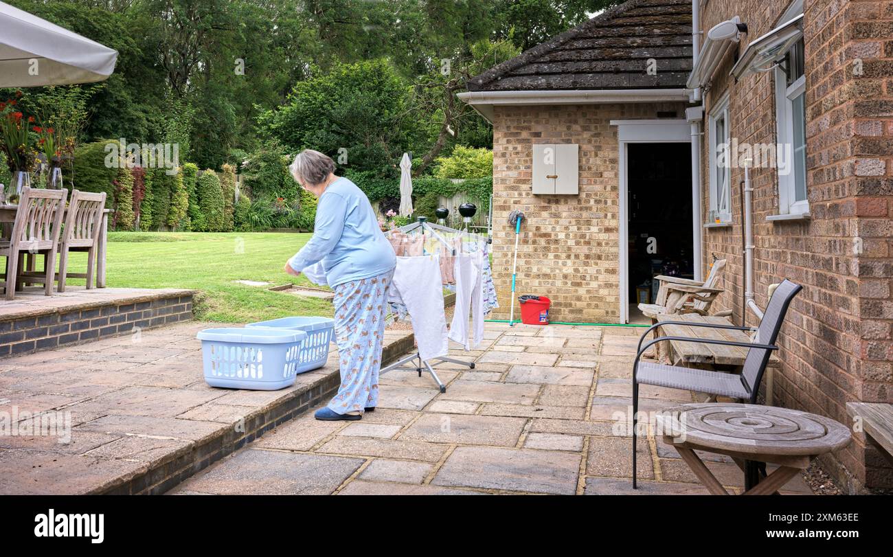 Eine Frau sortiert ihre Wäsche auf einer Terrasse in einem englischen Garten an einem sonnigen Sommertag. Stockfoto