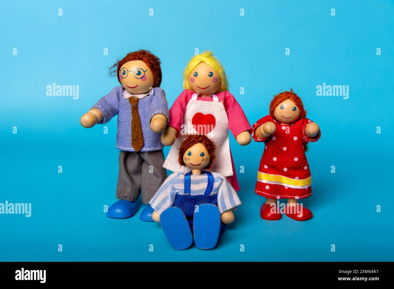 Eine vierköpfige Holzspielzeugfamilie – Vater, Mutter, Sohn und Tochter – wurde vor blauem Hintergrund angeordnet. Ideal für die Darstellung von Familiendynamik und Kindheit Stockfoto