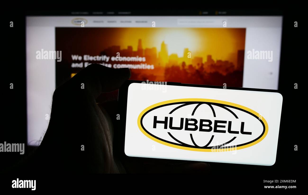 Person, die ein Mobiltelefon mit dem Logo des amerikanischen Elektronikunternehmens Hubbell Incorporated vor der Business-Webseite hält. Schwerpunkt auf dem Display des Telefons. Stockfoto