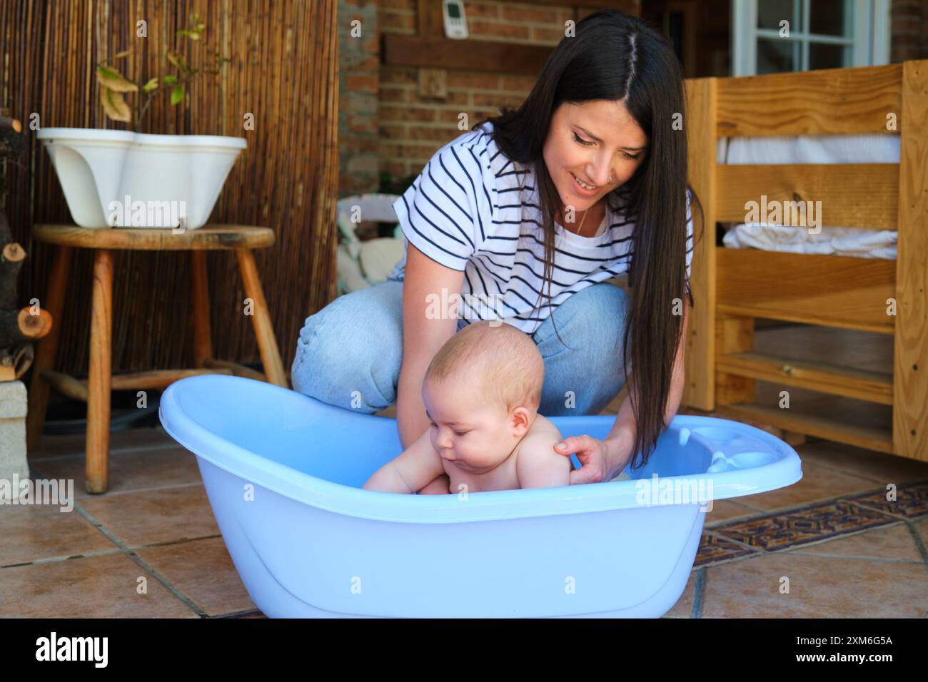 Mutter wäscht ihr Baby in einer blauen Badewanne auf der Terrasse Stockfoto