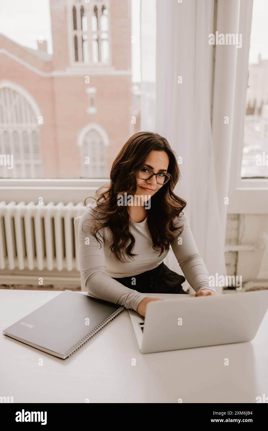 Hispanische Frau, die an einem weißen, modernen Schreibtisch mit Laptop und Notebook arbeitet Stockfoto