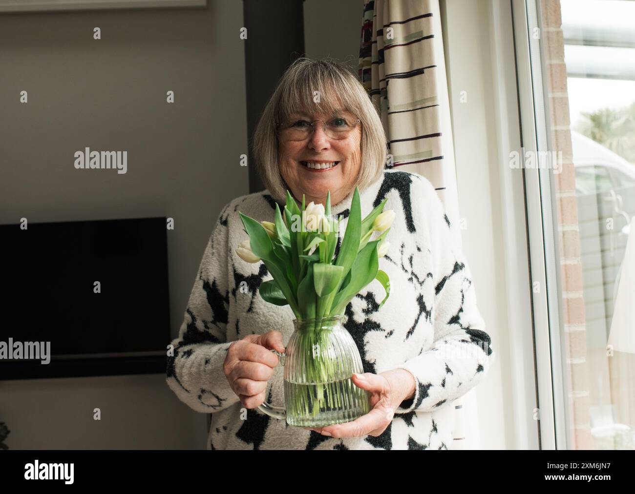 oma hält Blumen in einer Vase an ihrem Geburtstag Stockfoto