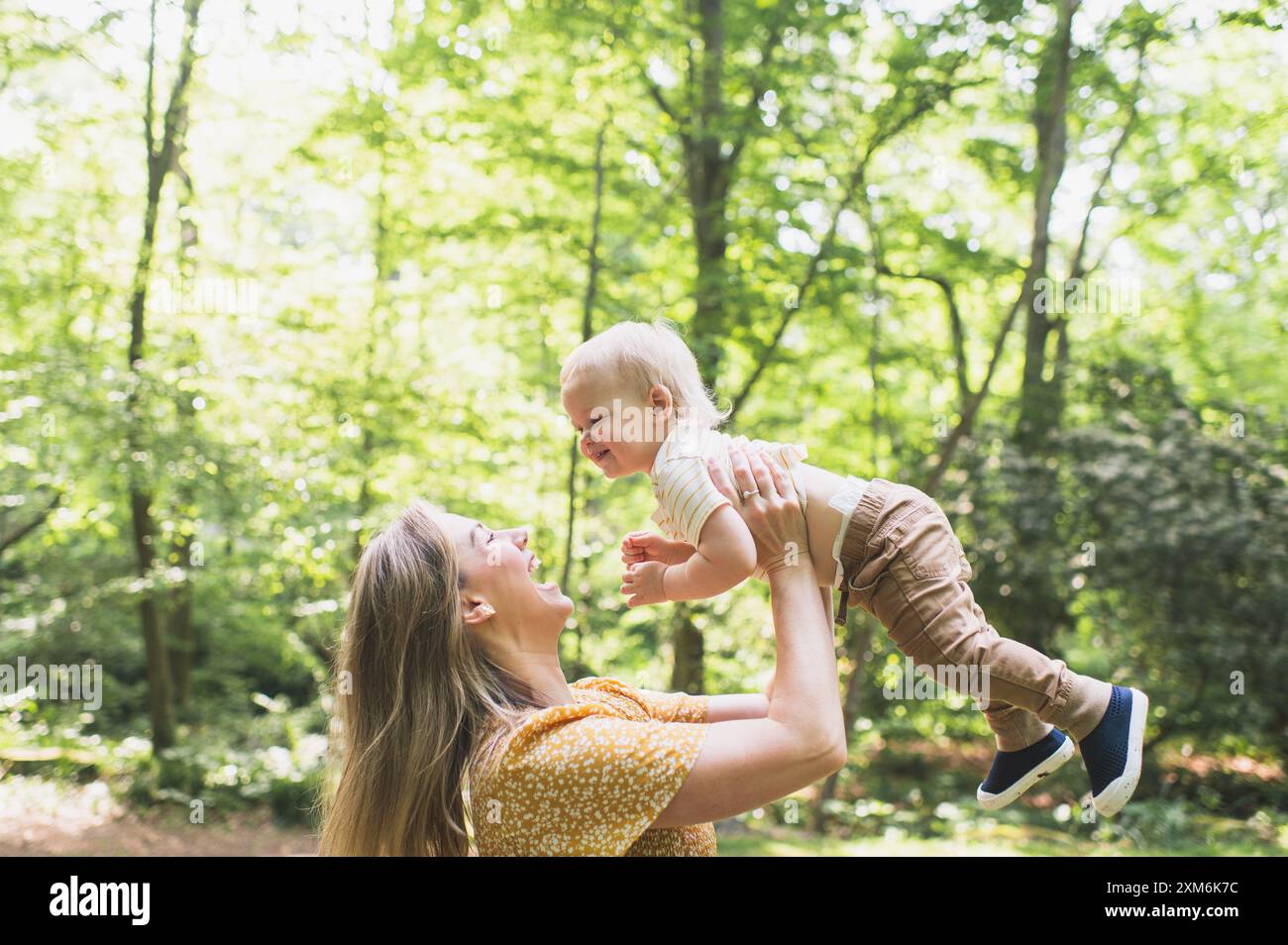 Mom lächelt Kleinkind an, während sie ihn in der Luft hält. Stockfoto