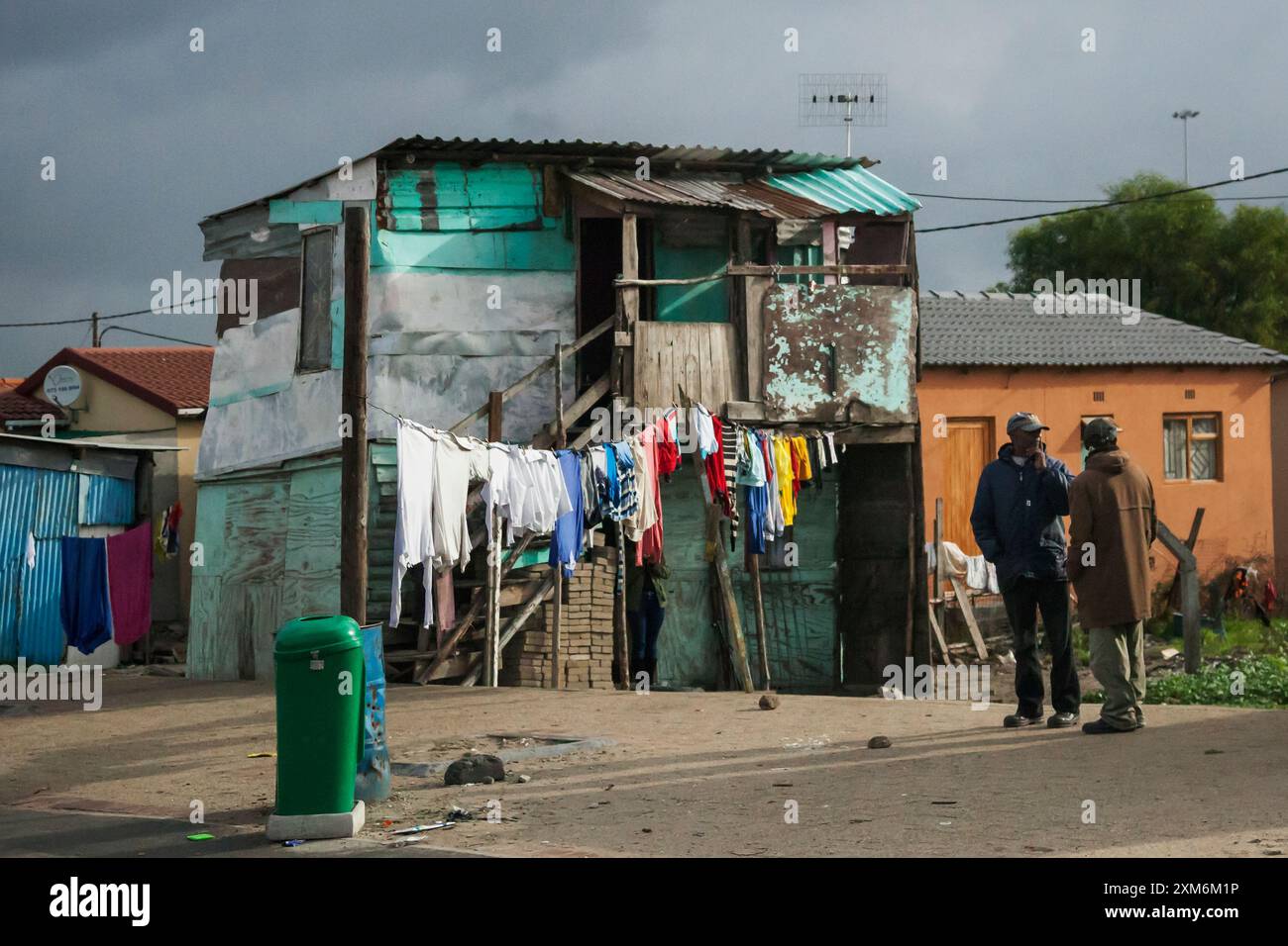 Zwei Männer plaudern vor einer bunten Kleiderschnur in einem Kapstadt Township Stockfoto