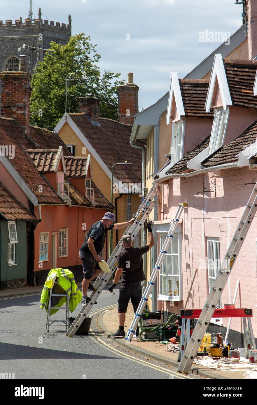 Zwei Arbeiter steigen Leitern auf einer angenehmen Renovierung eines Cottages in der Castle Street Framlingham mit dem Kirchturm von St. Michael's im Hintergrund. Stockfoto